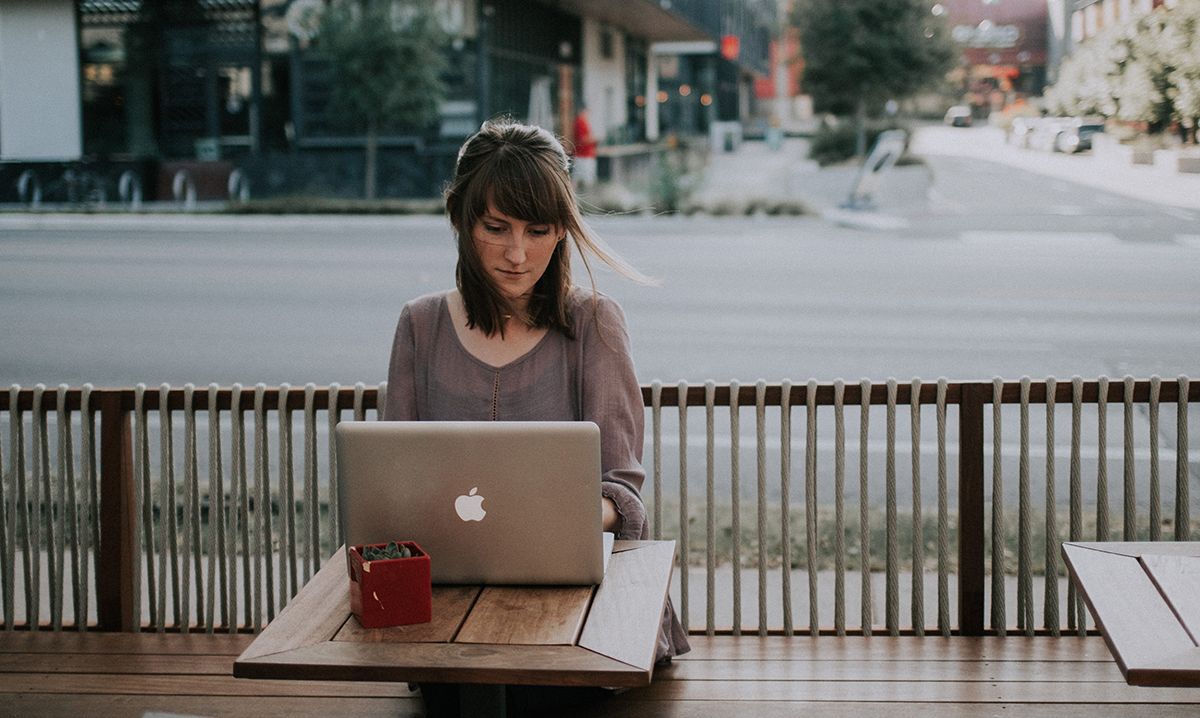 Photograph of a lady working on her laptop on a balcony outside a coffee shop